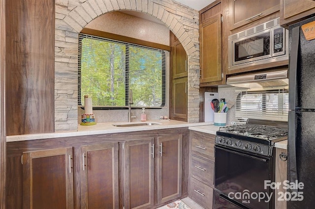 kitchen featuring black appliances, backsplash, light countertops, and a sink