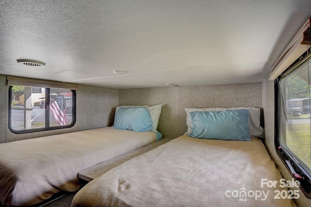 bedroom with multiple windows, a textured ceiling, and wallpapered walls