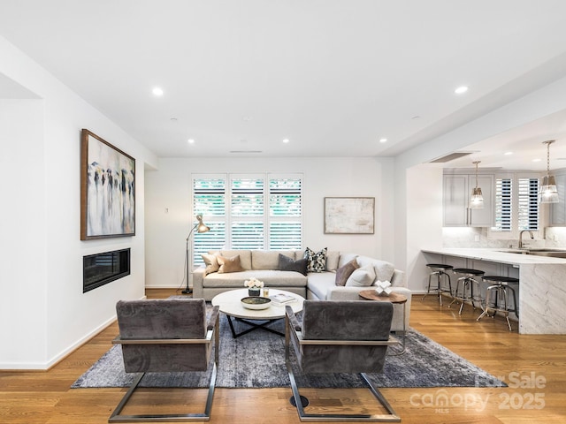 living room featuring light wood-type flooring, baseboards, a wealth of natural light, and a glass covered fireplace