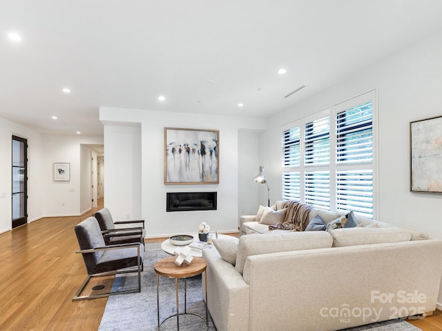 living room featuring baseboards, light wood finished floors, a glass covered fireplace, and recessed lighting