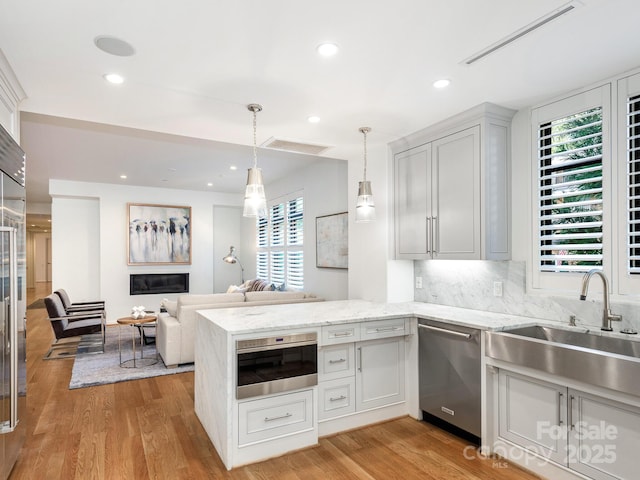 kitchen featuring decorative light fixtures, light wood finished floors, stainless steel dishwasher, a sink, and a peninsula