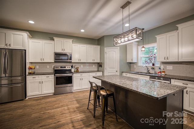 kitchen with appliances with stainless steel finishes, a sink, white cabinets, and a kitchen breakfast bar