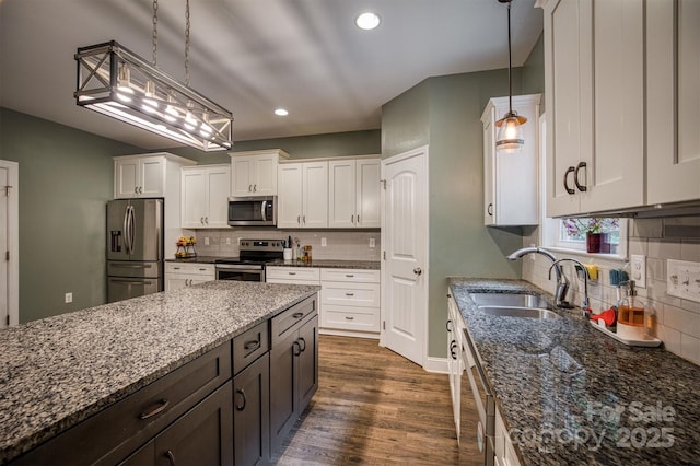 kitchen featuring appliances with stainless steel finishes, dark wood-type flooring, white cabinets, a sink, and dark stone counters