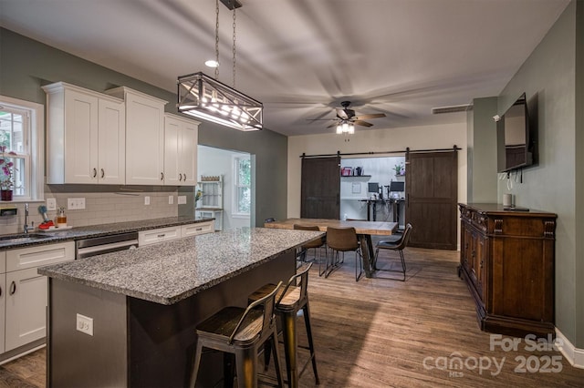 kitchen with a barn door, dark wood-style flooring, a kitchen island, white cabinets, and tasteful backsplash