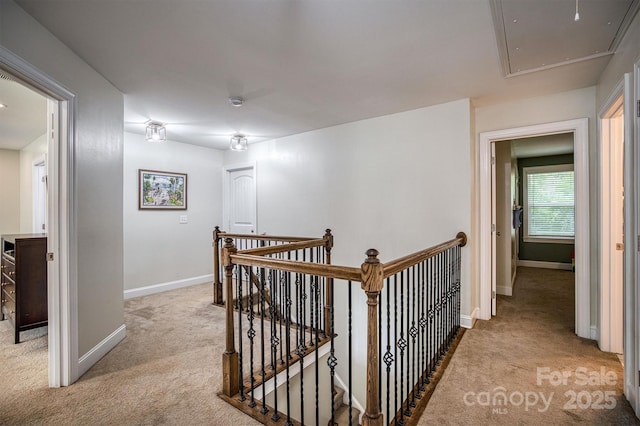 hallway featuring attic access, baseboards, light carpet, and an upstairs landing