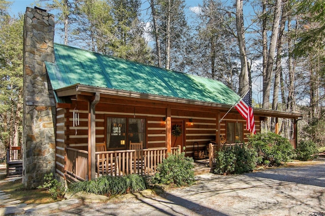 log-style house featuring metal roof, a chimney, a porch, and log exterior