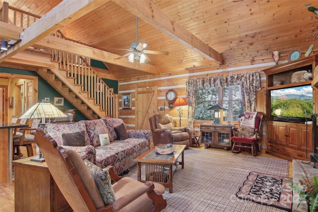 living room featuring wood walls, wood ceiling, a ceiling fan, stairway, and beamed ceiling