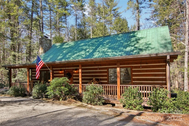 log home featuring covered porch, a chimney, and metal roof