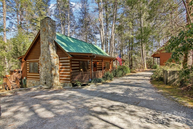 view of side of property featuring a porch, gravel driveway, metal roof, and a chimney