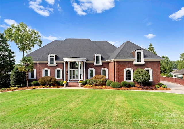 french country inspired facade featuring roof with shingles, a front lawn, and brick siding