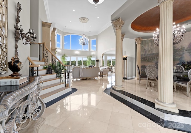 foyer entrance featuring a towering ceiling, ornamental molding, a chandelier, ornate columns, and stairs