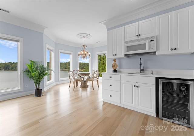 kitchen with wine cooler, white microwave, a sink, visible vents, and light countertops