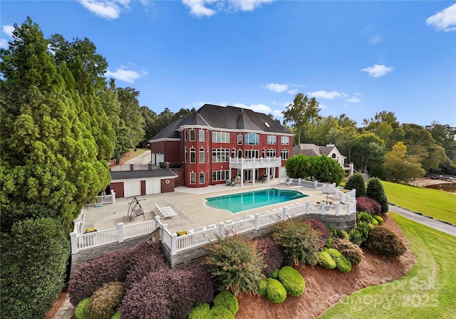 rear view of house featuring an outdoor pool, a balcony, a fenced backyard, a yard, and a patio area