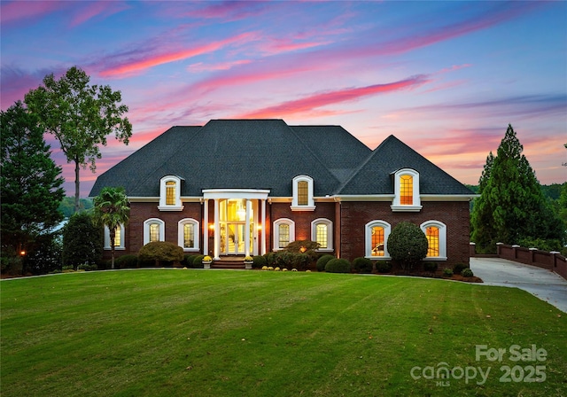 french country style house featuring concrete driveway, brick siding, a lawn, and roof with shingles