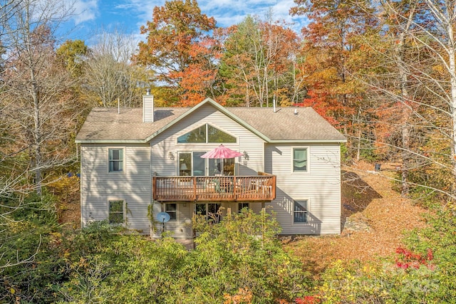 rear view of house with a chimney, a deck, and roof with shingles