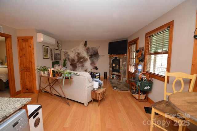 living area featuring light wood-style floors, a wall mounted air conditioner, a fireplace, and baseboards