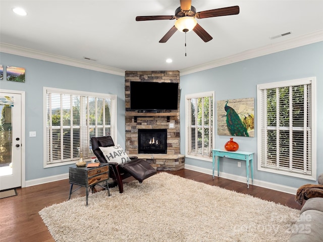 living room featuring baseboards, ornamental molding, wood finished floors, and a stone fireplace