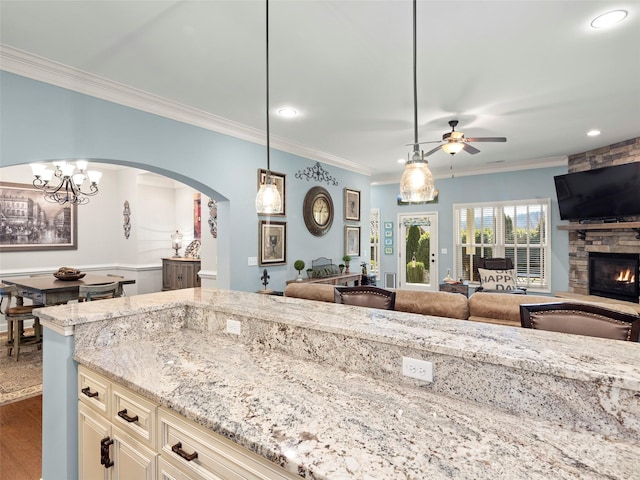 kitchen featuring light stone counters, open floor plan, cream cabinets, crown molding, and a stone fireplace