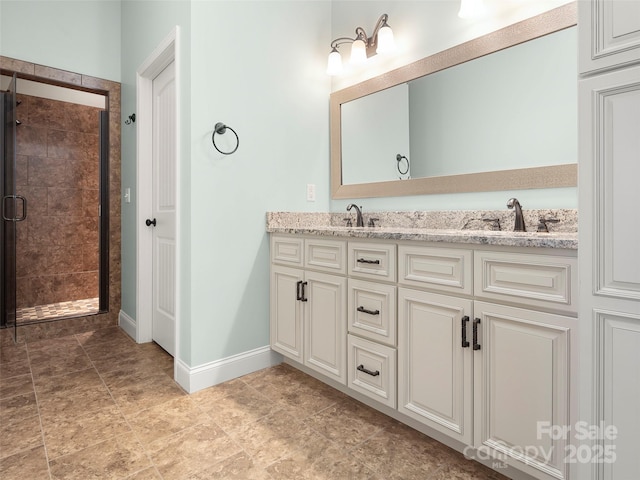 full bath with double vanity, a stall shower, baseboards, and a sink