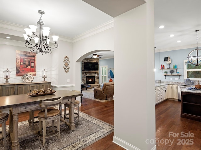 dining area with crown molding, arched walkways, dark wood finished floors, and a stone fireplace