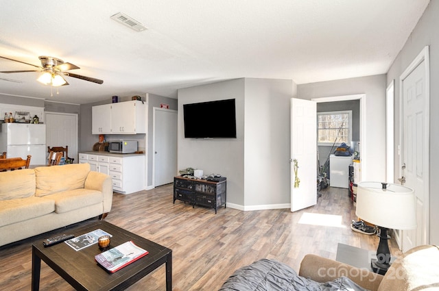 living area with baseboards, a ceiling fan, visible vents, and light wood-style floors