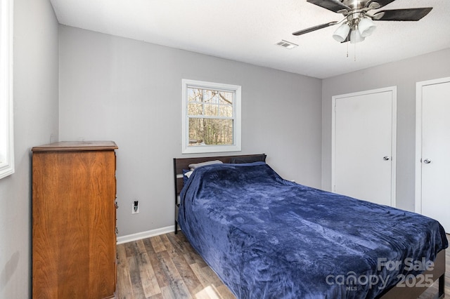 bedroom featuring a ceiling fan, wood finished floors, visible vents, and baseboards