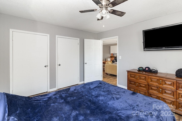 carpeted bedroom with baseboards, a textured ceiling, a ceiling fan, and two closets