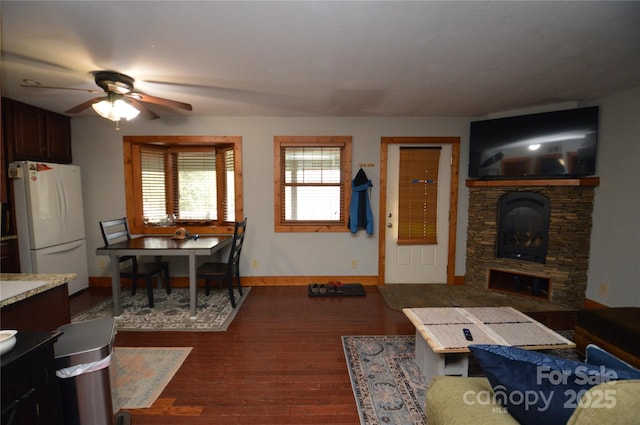 living area with a fireplace, baseboards, dark wood finished floors, and a ceiling fan