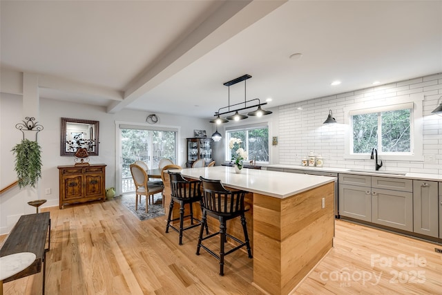 kitchen with backsplash, a sink, light wood-style flooring, and gray cabinetry