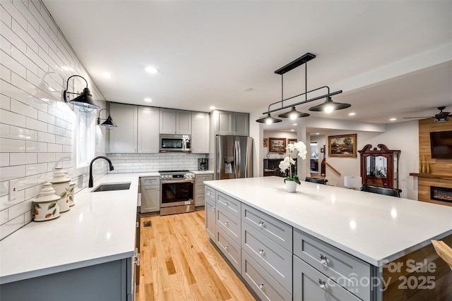 kitchen with appliances with stainless steel finishes, gray cabinets, a large fireplace, and a sink