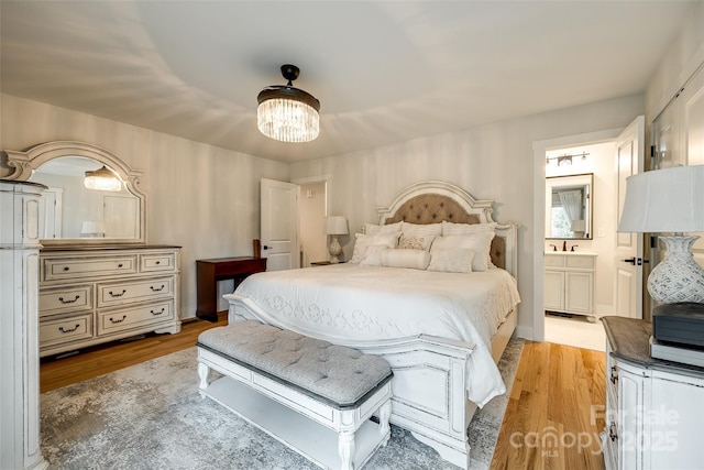 bedroom with light wood-type flooring, connected bathroom, a sink, and an inviting chandelier