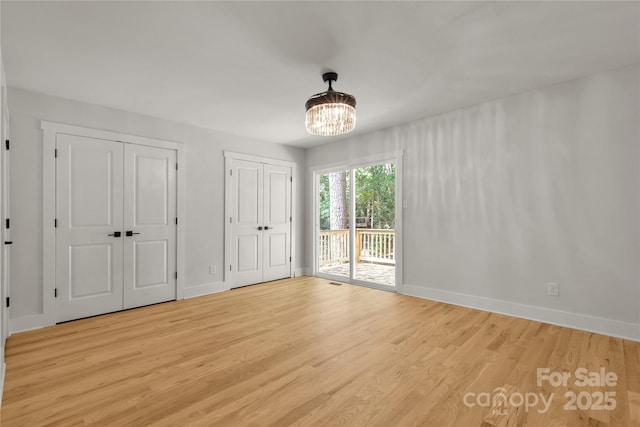 unfurnished bedroom with baseboards, access to exterior, light wood-type flooring, a chandelier, and multiple closets