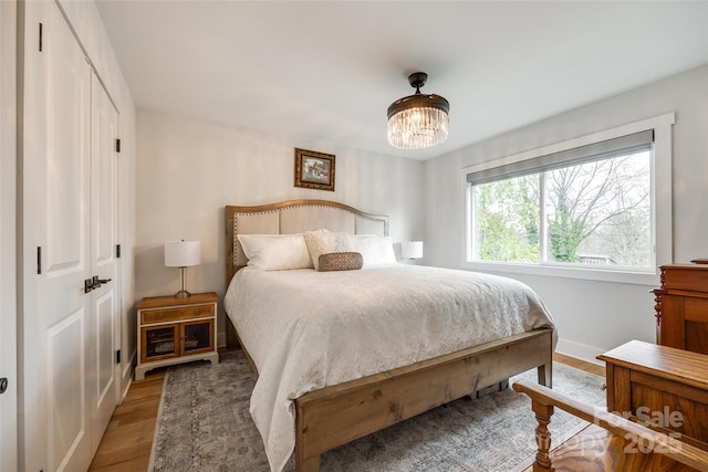 bedroom with a closet, an inviting chandelier, wood finished floors, and baseboards