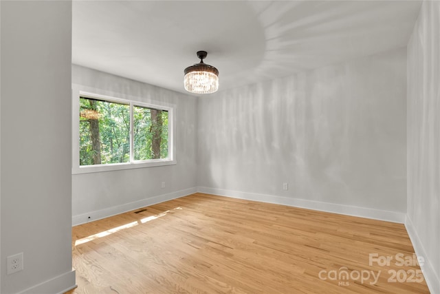 empty room featuring baseboards, light wood finished floors, and a notable chandelier