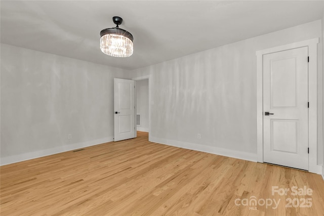 spare room with light wood finished floors, baseboards, and a notable chandelier