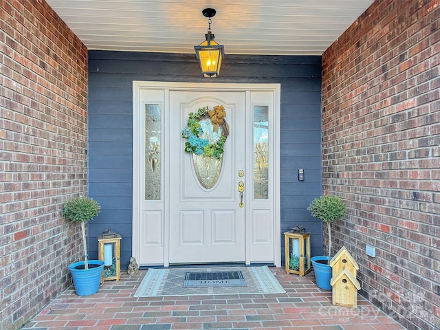 doorway to property featuring covered porch and brick siding