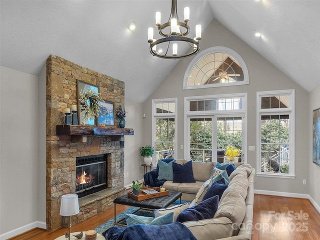 living area featuring a chandelier, high vaulted ceiling, a stone fireplace, wood finished floors, and baseboards