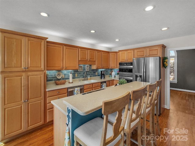 kitchen with light wood-style flooring, stainless steel appliances, light countertops, a kitchen bar, and backsplash