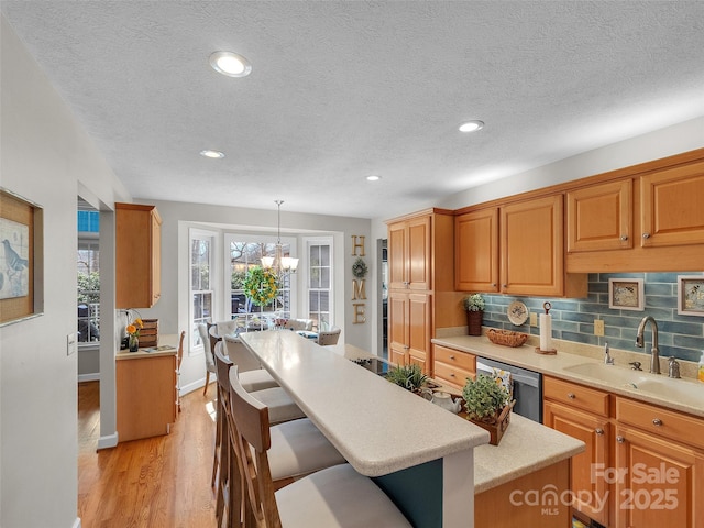 kitchen with a breakfast bar, light wood finished floors, light countertops, a chandelier, and dishwasher