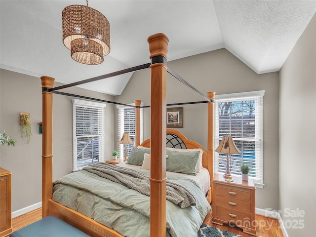 bedroom with baseboards, an inviting chandelier, vaulted ceiling, a textured ceiling, and light wood-type flooring