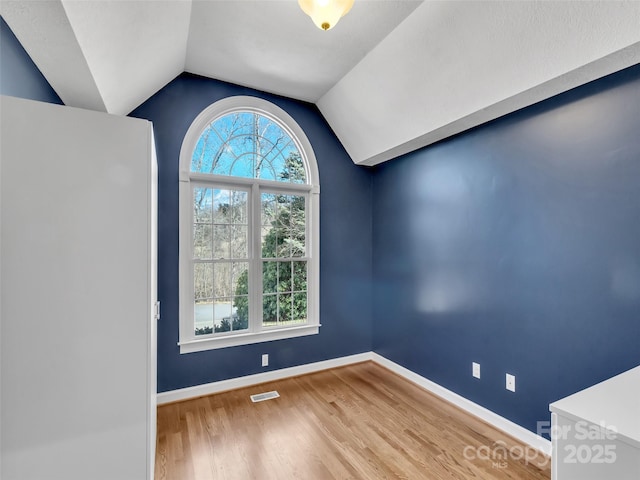 spare room with lofted ceiling, wood finished floors, visible vents, and baseboards