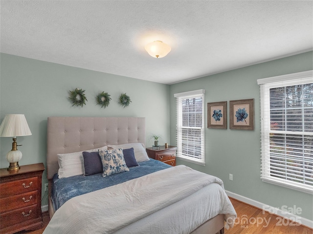 bedroom with a textured ceiling, wood finished floors, and baseboards