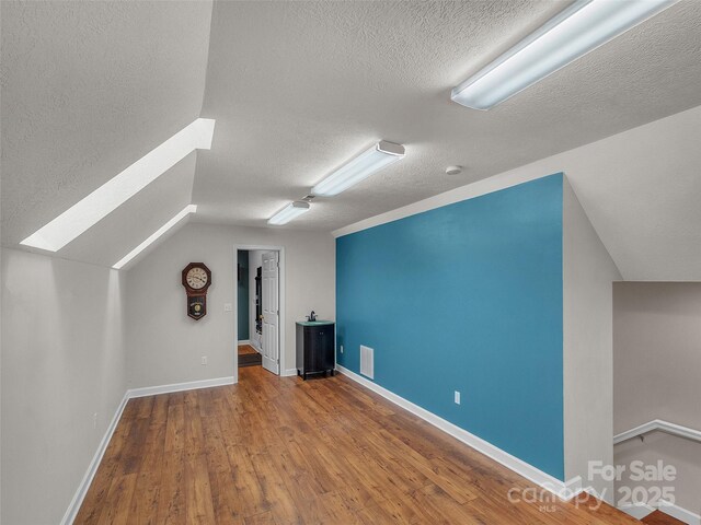 bonus room with a textured ceiling, baseboards, vaulted ceiling, and wood finished floors