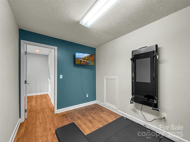 exercise area featuring a textured ceiling, light wood finished floors, and baseboards