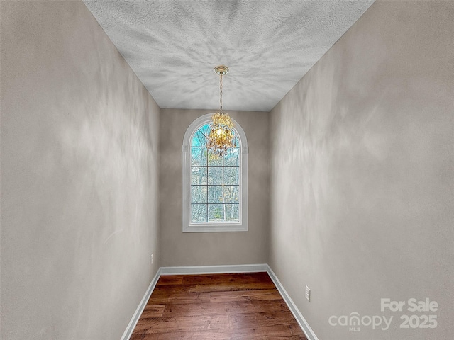 unfurnished dining area with a chandelier, dark wood finished floors, and baseboards