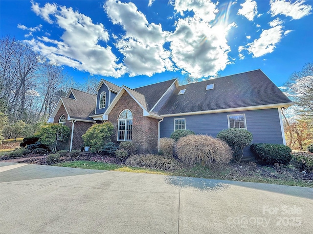 traditional home featuring roof with shingles and brick siding