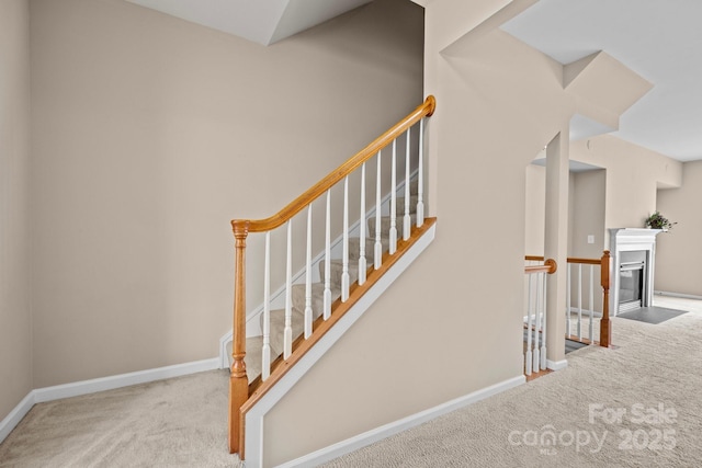 staircase with a fireplace with flush hearth, carpet, and baseboards