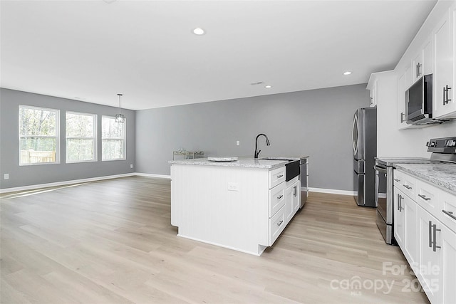 kitchen with light wood-style flooring, a sink, white cabinets, appliances with stainless steel finishes, and an island with sink