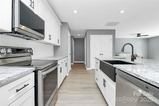 kitchen featuring visible vents, appliances with stainless steel finishes, light stone countertops, light wood-style floors, and a sink