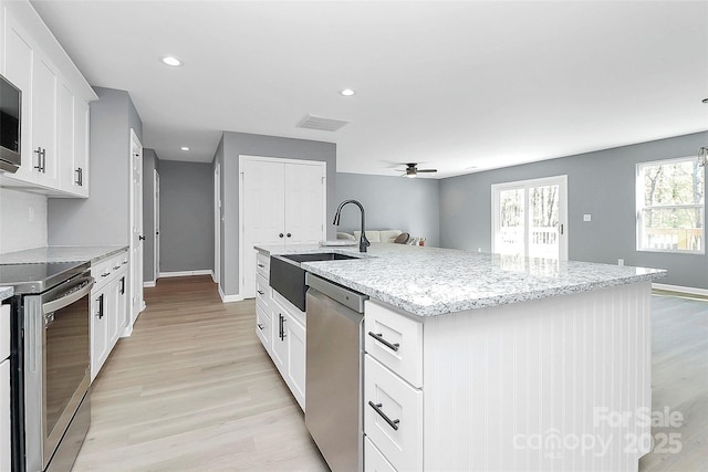 kitchen featuring light wood-style flooring, appliances with stainless steel finishes, light stone counters, a kitchen island with sink, and a sink